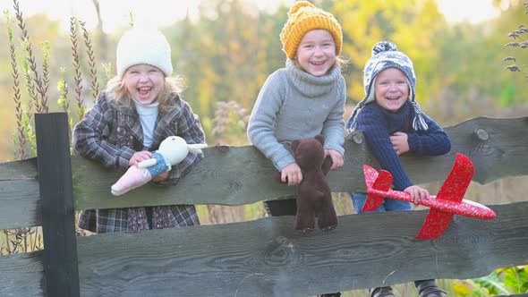 Group of joyful children with toys on a wooden fence.