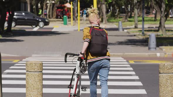 Albino african american man with dreadlocks crossing street with bike alt