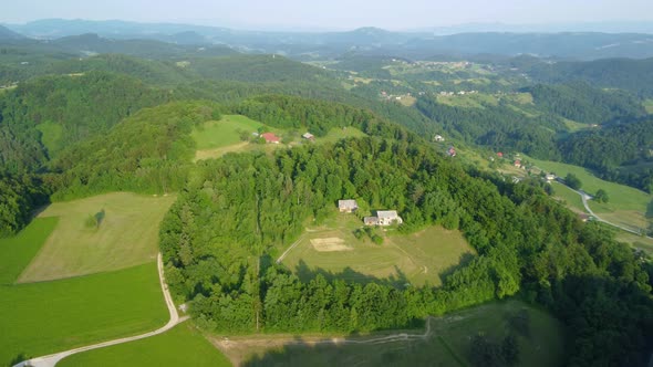 Hill lands covered with green forests and meadows full of family houses and farms. Aerial 4k view. alt