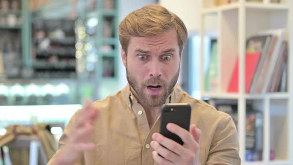 Portrait of Young Man Reacting to Loss on Smartphone alt