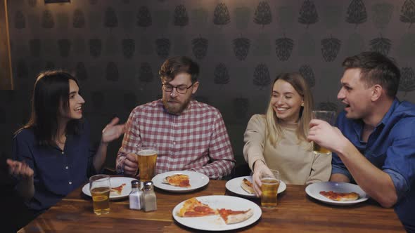Happy Friends Sit at the Table in Pub Eat Pizza Watch Tv and Talk with Each Other