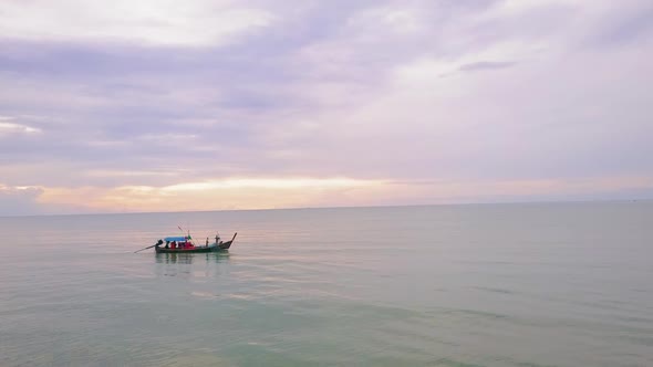 Drone view of a long tail boat on the ocean with a sunset in the background alt