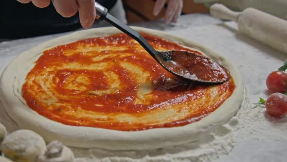 Chef is Spreading Tomato Sauce on Pizza Dough