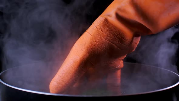 A hand in orange thermal glove inside boiling water