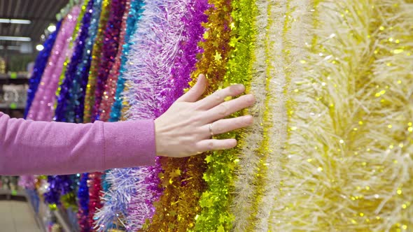 Girl Holds Her Hand on the Christmas Garlands in the Store