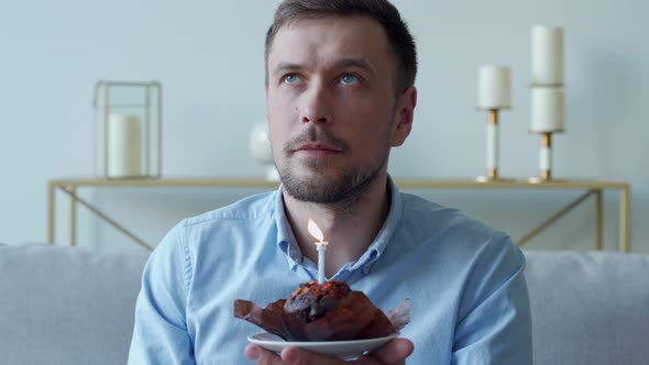 Man Sitting on the Sofa Blows Out the Candles on the Cake alt