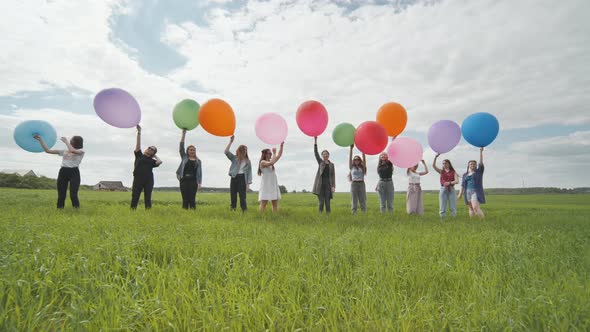 Cheerful Girls are Standing on the Field with Large Balloons and Colorful Balloons alt
