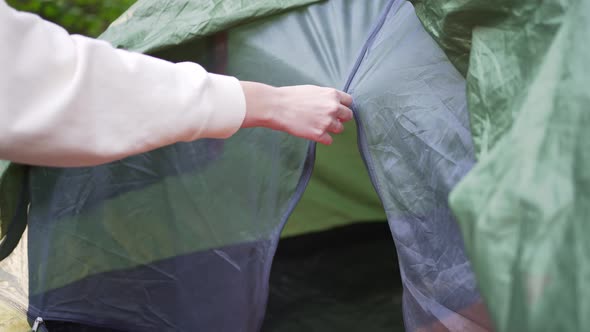 A Woman Closes the Clasp of a Tent in a Forest Campsite