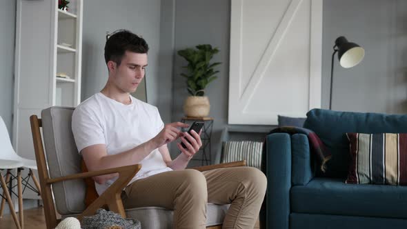 Man Text Messaging on Smartphone, Sitting on Couch alt