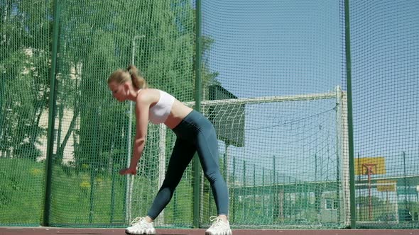 Young Sporty Blond Girl in Sportswear Does Exercises Outdoors at Sports Ground