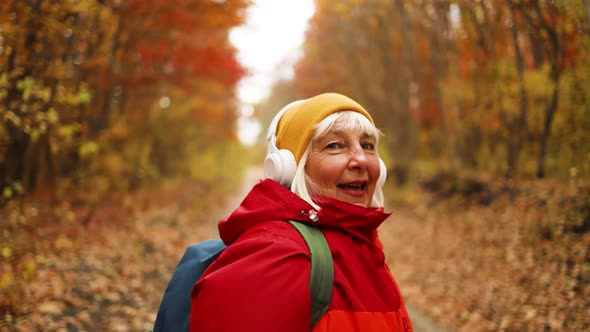 Cheerful Active 50s Woman Walking Along with Headphones Mobile Phone and Backpack Enjoying Listening