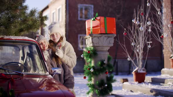 Happy Girls Standing Near Red Car Eating Sweet Lollipops Wintertime alt