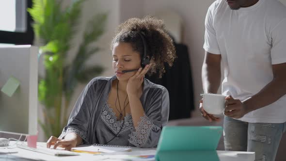 Young African American Man Bringing Coffee Cup for Tired Overworking Woman Messaging Online From alt