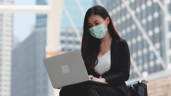 Business girl with mask use laptop outdoor with day light and she action of get good idea alt