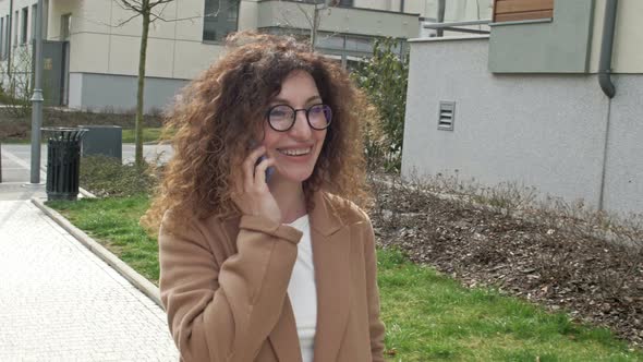 Curlyhaired Woman Middleaged in Glasses Walks Along a Deserted City Street