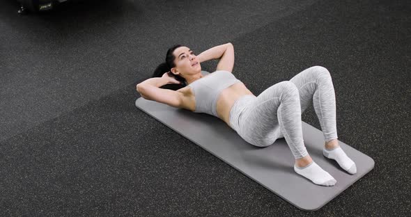 A Young Athletic Woman Does an Exercise on the Abdominal Press Lies on the Floor in the Gym Dressed
