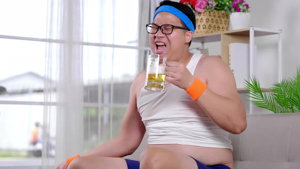 Funny fat Asian guy in sportswear doing exercise weight training by dumbbell and drinking beer alt