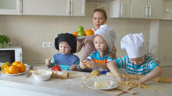 Mom Teaches Kids To Cook. Children Kneading Dough in the Kitchen and Smeared in Flour.
