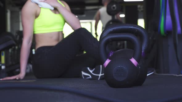 Fitness Woman Resting After Workout at the Gym, Kettlebells on the Foreground alt