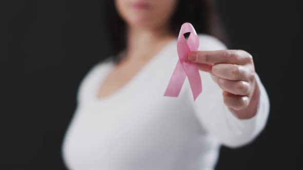 Mid section of woman holding a pink ribbon against black background alt