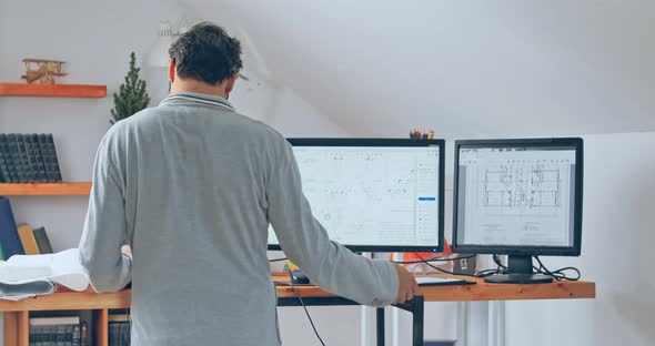 A Back View of a Man with Glasses Working at a Laptop and with Two Additional Monitors Above the alt