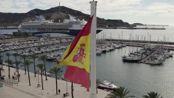 Close up of Spanish flag waving in the wind with Cartagena touristic port and cruise ship in backgro