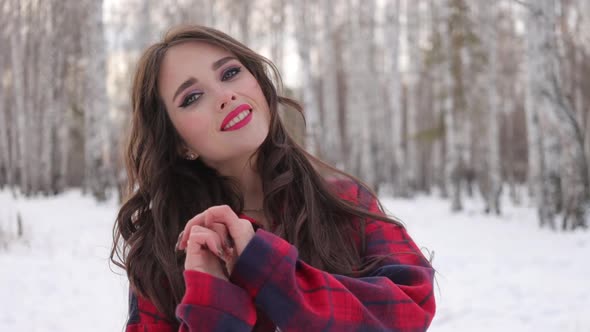 Young Woman with Wavy Hair Standing and Touching Face in Winter Forest