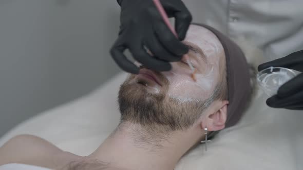 Unrecognizable Beauty Therapist Using Brush Applying White Enzyme Peel on Face Skin of Male Client alt