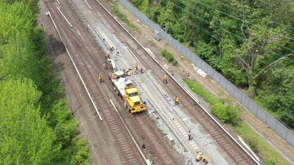 an aerial view over workers repairing train tracks on a sunny morning. The drone camera tilted down alt
