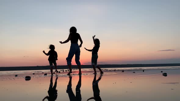 Happy family are jumping, dancing at sunset in the water. Traveling with your family to nature.