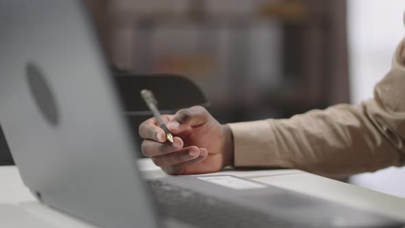 Black Man is Making Notes on Paper During Mobile Call Sitting at Table in Office or Working Room alt