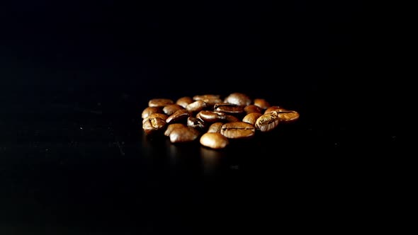 Roasted coffee grains scatter on a black background. Close-up of coffee beans.