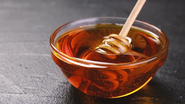 Honey in glass jar with honey dipper over black background