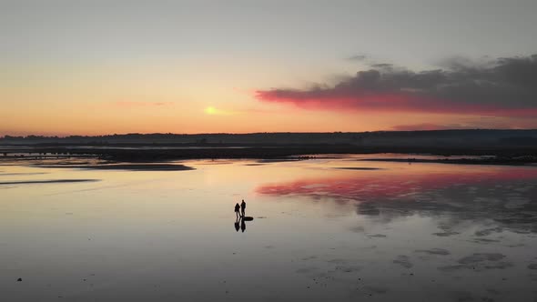 couple standing on a reflecting lake at sundown silhouette aerial