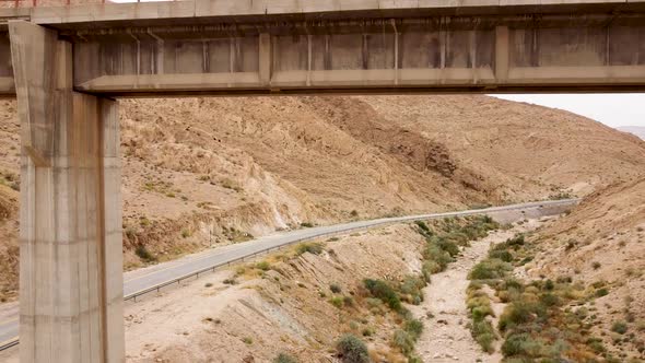 aerial slow backward drone shot under empty train bridge, revealing the mountains, an empty side roa alt