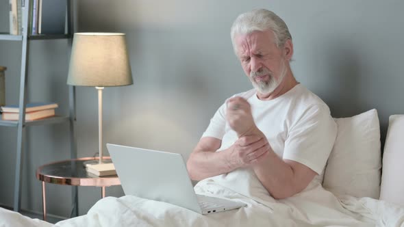 Old Man with Laptop Having Wrist Pain in Bed  alt