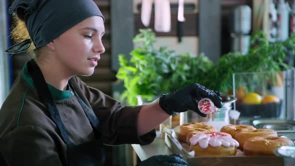 Charming Pastry Chef Girl Working in Kitchen of Bakery and Decorating Sweet Fried Donuts with alt