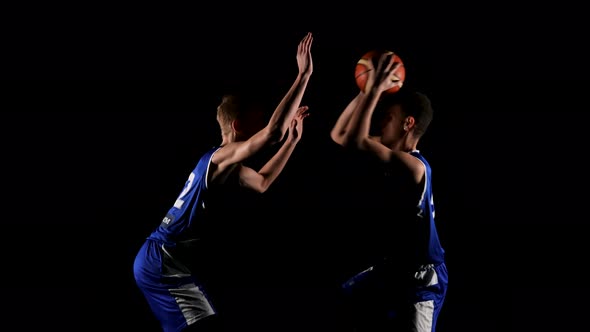 Two Young Sportsmen are Practicing Basketball in a Dark Studio on a Black Background alt