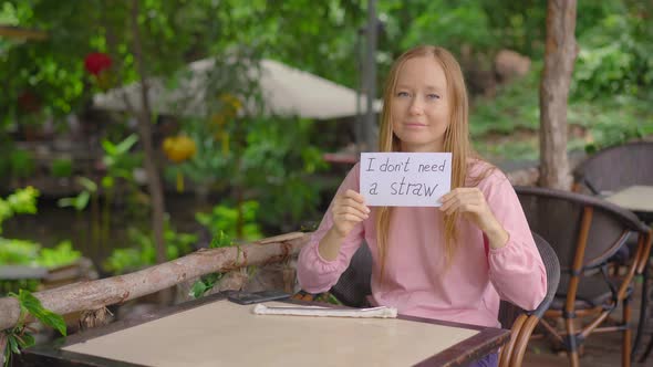 In a Cafe, a Young Woman Refuses To Take a Single-use Plastic Drinking Straw. She Is Holding a Paper alt