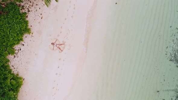 Aerial Vertical Move Up Footage From Girl Doing Sand Angel on White Tropical Beach alt