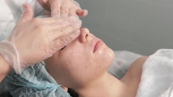 A Professional Cosmetologist Applies a Clear Cleansing Gel to the Client's Face