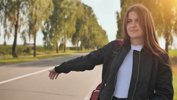 A Young Girl of 17 Years Old Stands on the Road and Tries to Stop Any Car alt