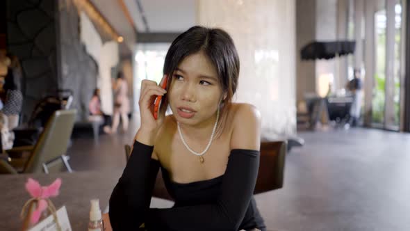 Slider Shot of Beautiful Young Asian Woman Who Talks on the Telephone Sitting on a Sofa in a Lounge alt