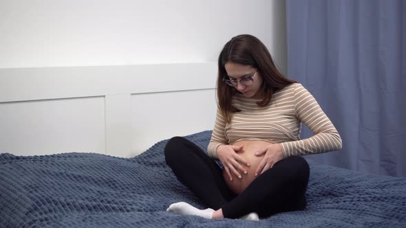 Young Pregnant Woman with Glasses Smears Cream on Her Belly alt