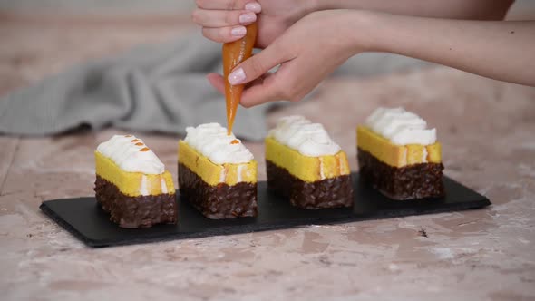 Female hands decorate a sponge cakes with apricot jam from a pastry bag.