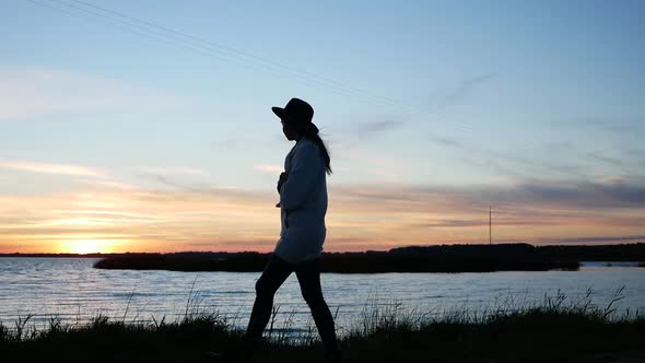 Girl in a Hat and a White Sweater at Sunset Walking alt