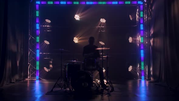 Silhouette Drummer Playing on Drum Kit on Stage in a Dark Studio with Smoke and Neon Lighting alt