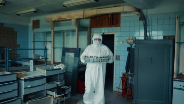 A laboratory assistant in a medical suit and medical mask enters the room
