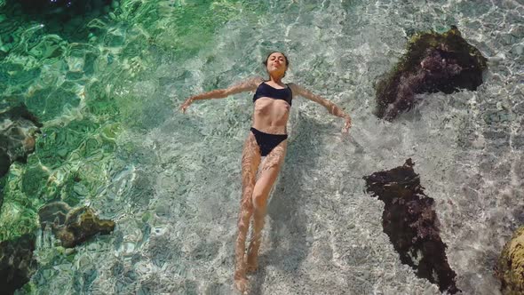 High Angle View of Relaxing Woman in Black Bikini with Perfect Body Floating in Blue Clear Sea Water alt