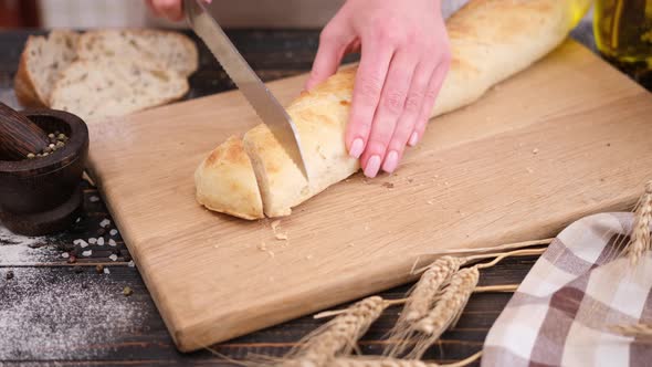 Woman Slicing Fresh Baguette Bread on Wooden Cutting Board alt